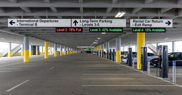 Large international airport parking structure with wayfinding signs, occupancy indicators, and EV charging stations
