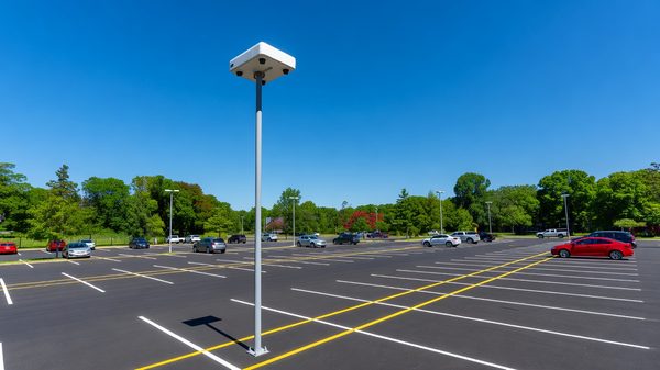 Overhead sensor unit mounted on a pole above marked parking bays in an open lot